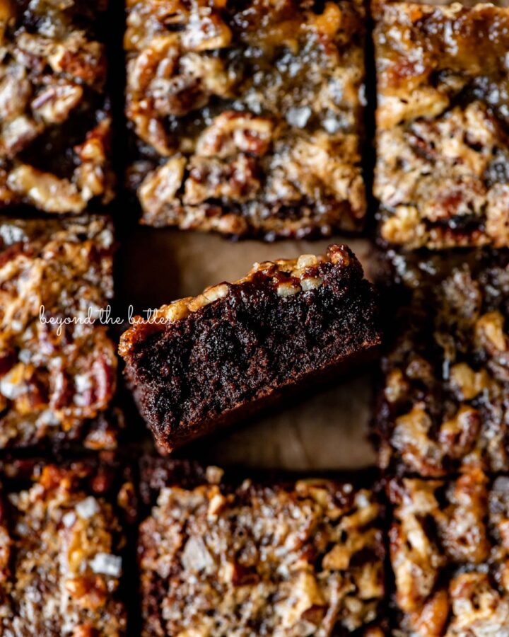 Salted pecan pie brownies placed on brown parchment paper with the center brownie placed on its side.