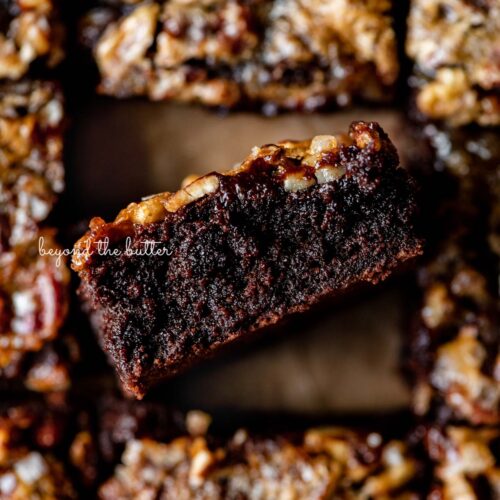Salted pecan pie brownies placed on brown parchment paper with the center brownie placed on its side on an angle.