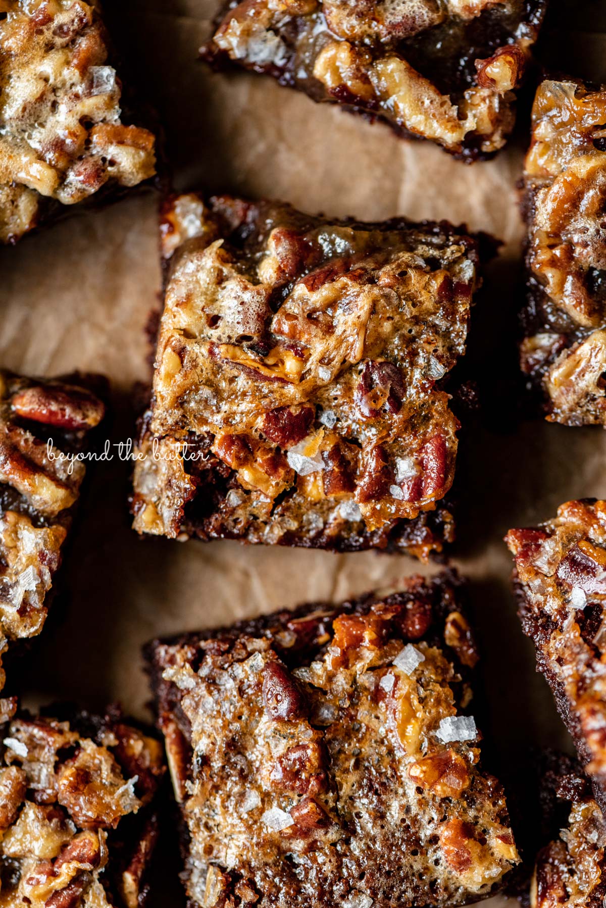 Salted pecan pie brownies placed on brown parchment paper | © Beyond the Butter®