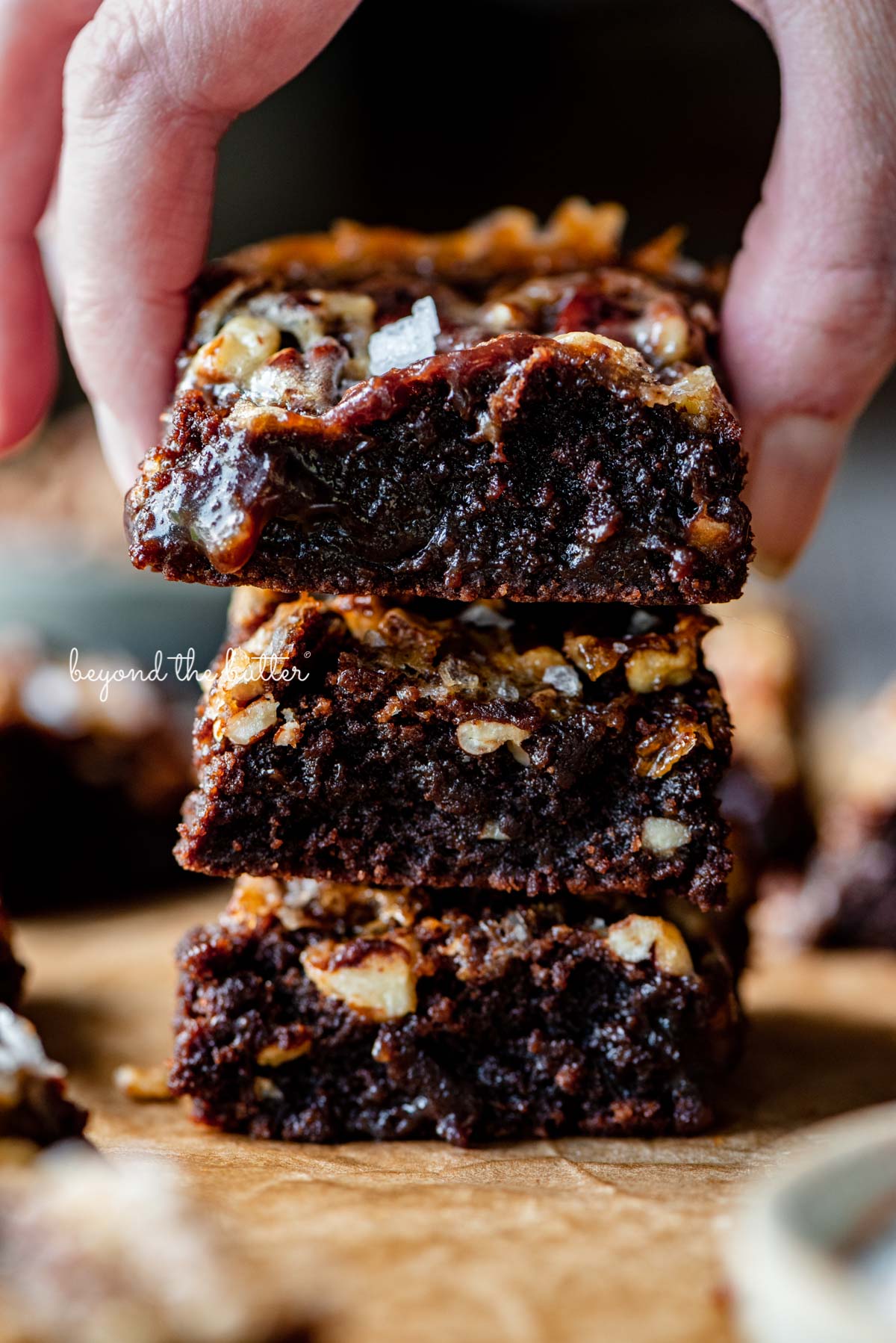 Stacking the best salted pecan pie brownies on brown parchment paper | © Beyond the Butter®