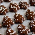 Close up image of Chocolate Dipped Graham Cracker Chrismtas Trees topped with white nonpareils on a wax paper lined baking sheet.
