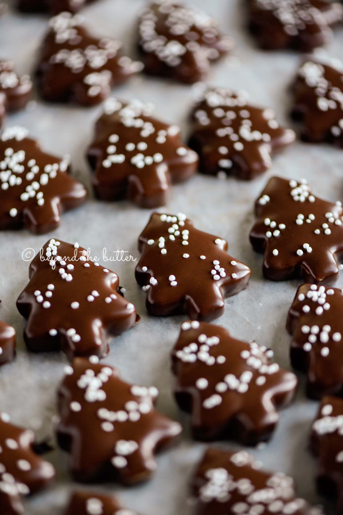 Close up image of Chocolate Dipped Graham Cracker Chrismtas Trees topped with white nonpareils on a wax paper lined baking sheet.