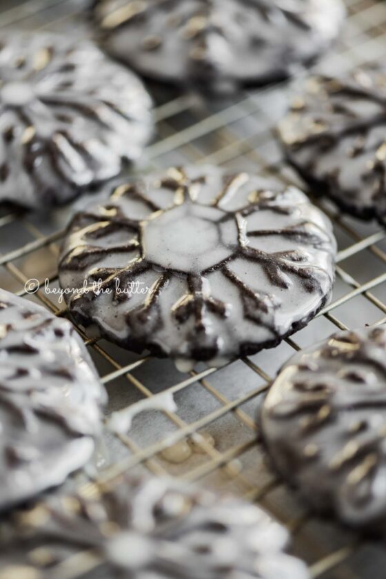 Angled closeup image of homemade oreo snowflake cookies on a wire cooling rack | All Images © Beyond the Butter®