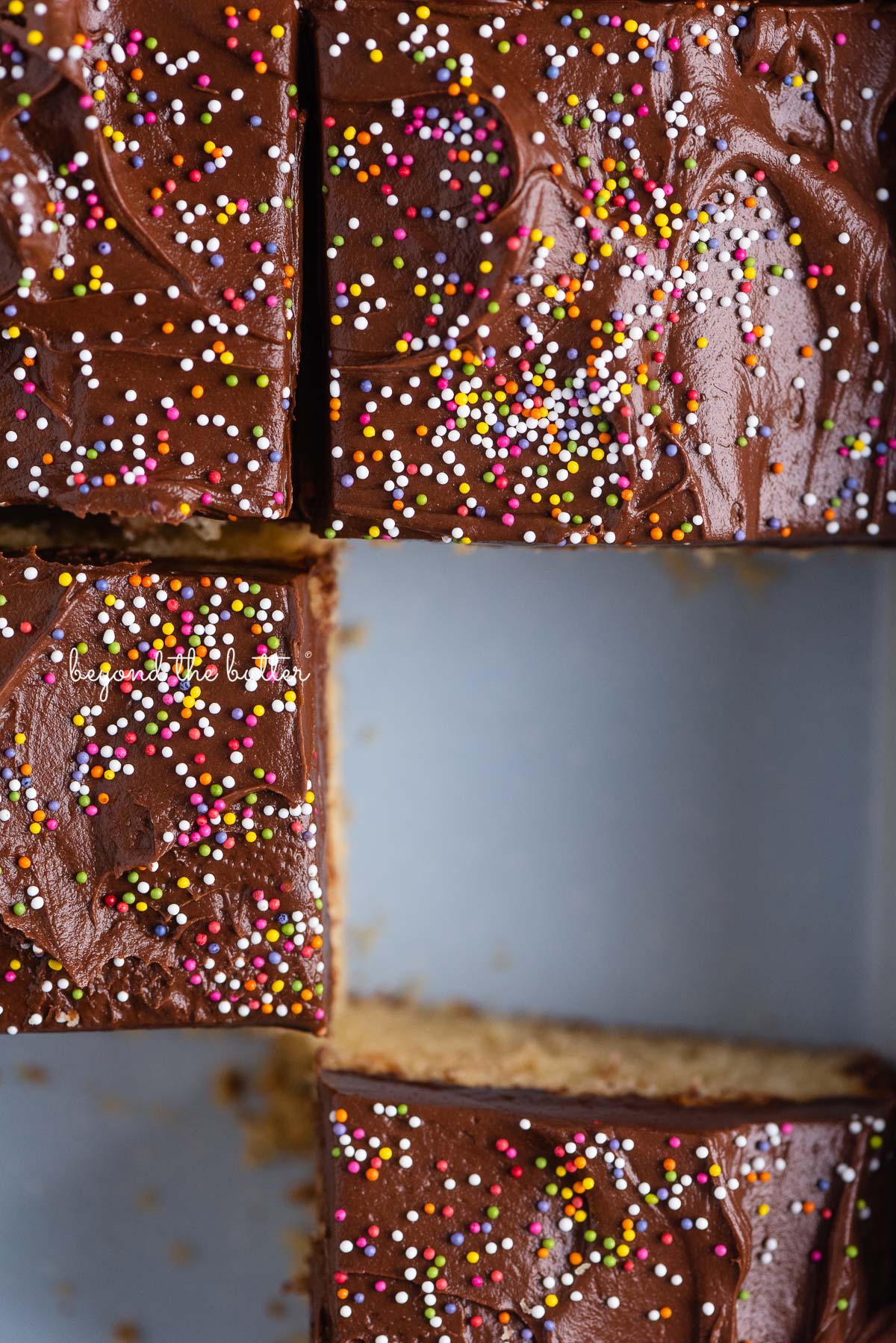 Slices of yellow sheet cake frosted with chocolate frosting and topped with rainbow nonpareils | © Beyond the Butter®