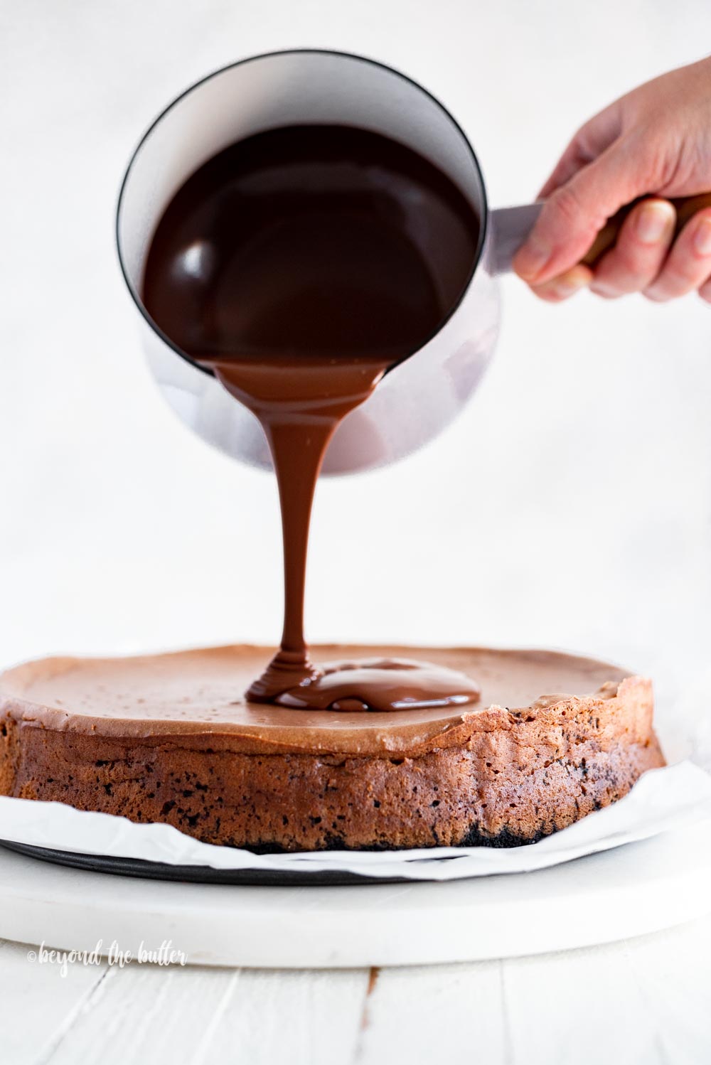 Pouring dark chocolate ganache over top of Triple Chocolate Mocha Cheesecake | All Images © Beyond the Butter, LLC
