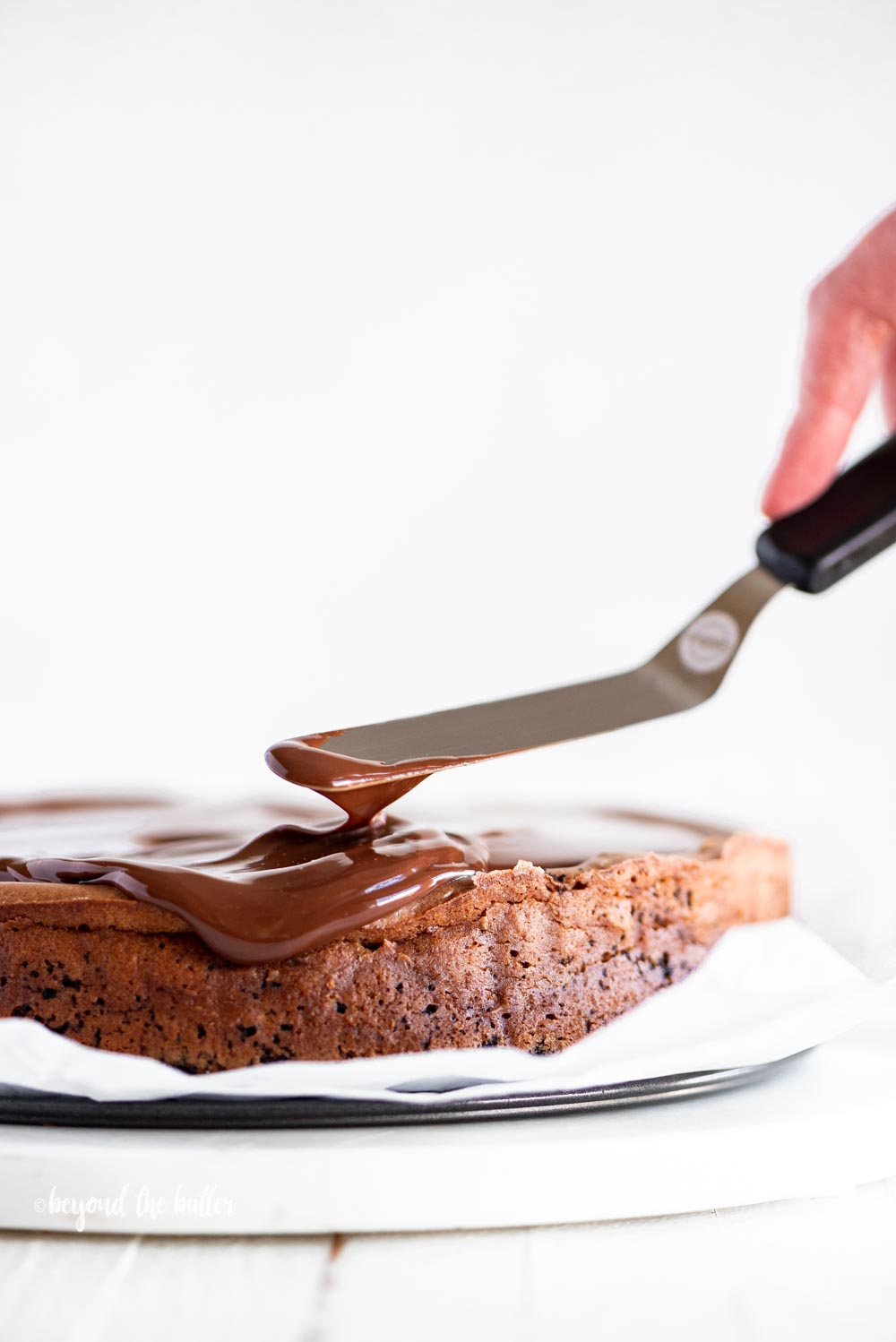 Using an offset spatula to spread out the dark chocolate ganache on top of the Triple Chocolate Mocha Cheesecake | All Images © Beyond the Butter, LLC