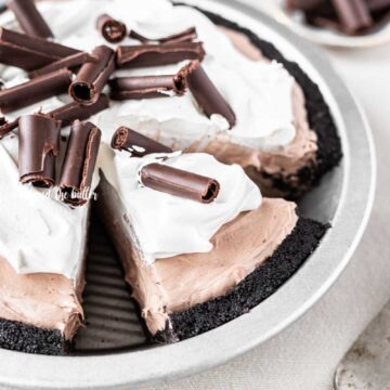 Angled image of sliced no-bake chocolate cream pie with chocolate wafer crust and garnished with Cool Whip and chocolate curls | All Images © Beyond the Butter™