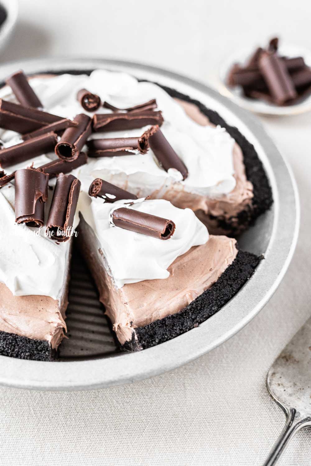 Angled image of sliced no-bake chocolate cream pie with chocolate wafer crust and garnished with Cool Whip and chocolate curls.