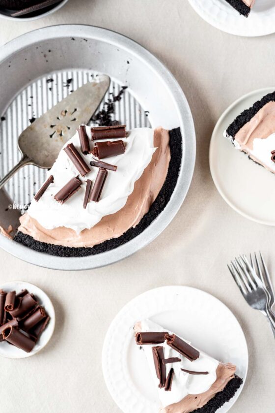 Overhead image of sliced no-bake chocolate cream pie with slices of pie on dessert plates next to it | All Images © Beyond the Butter™