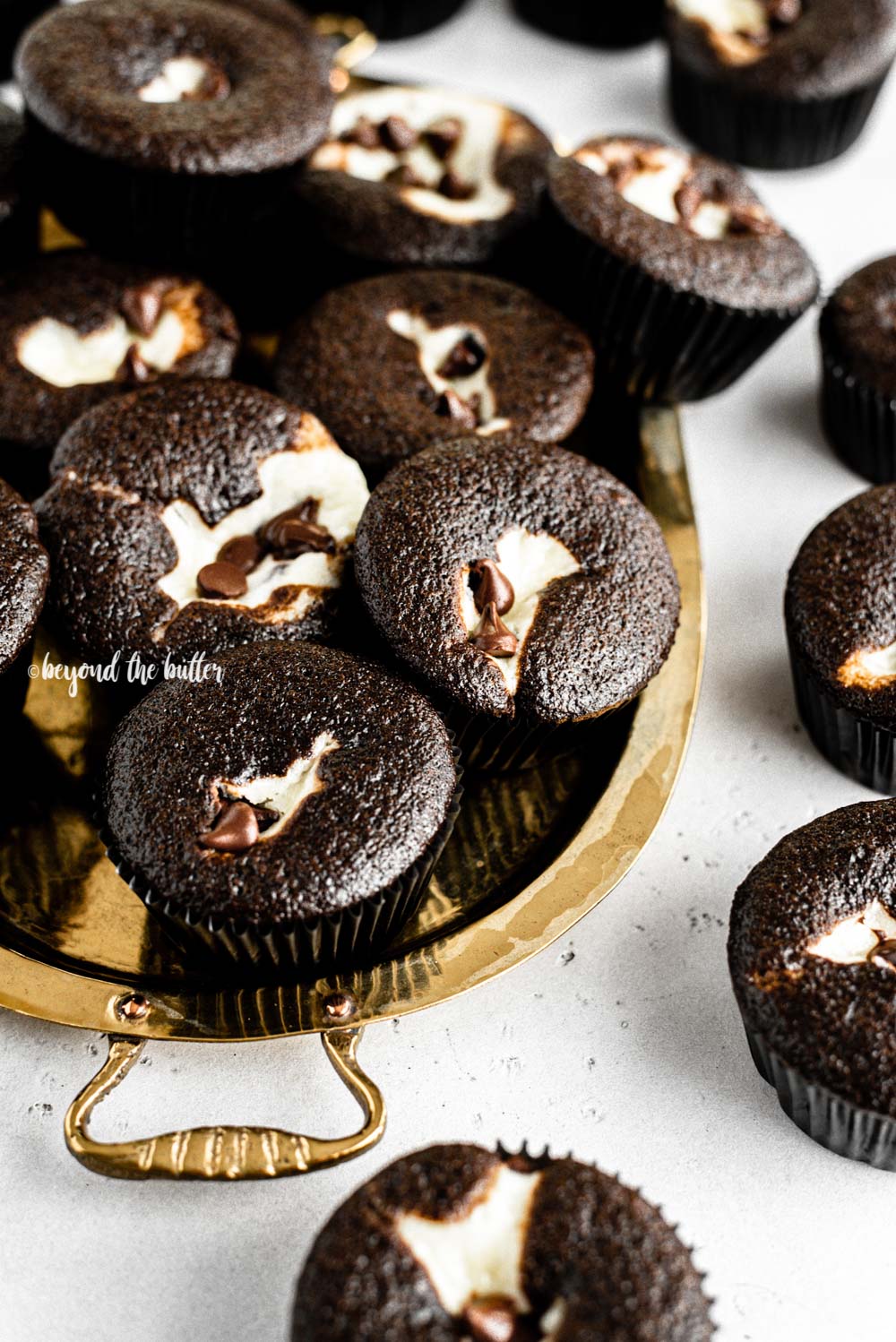 Close up angled image of black bottom cupcakes randomly placed on gold serving plate on a gray background | All Images © Beyond the Butter™