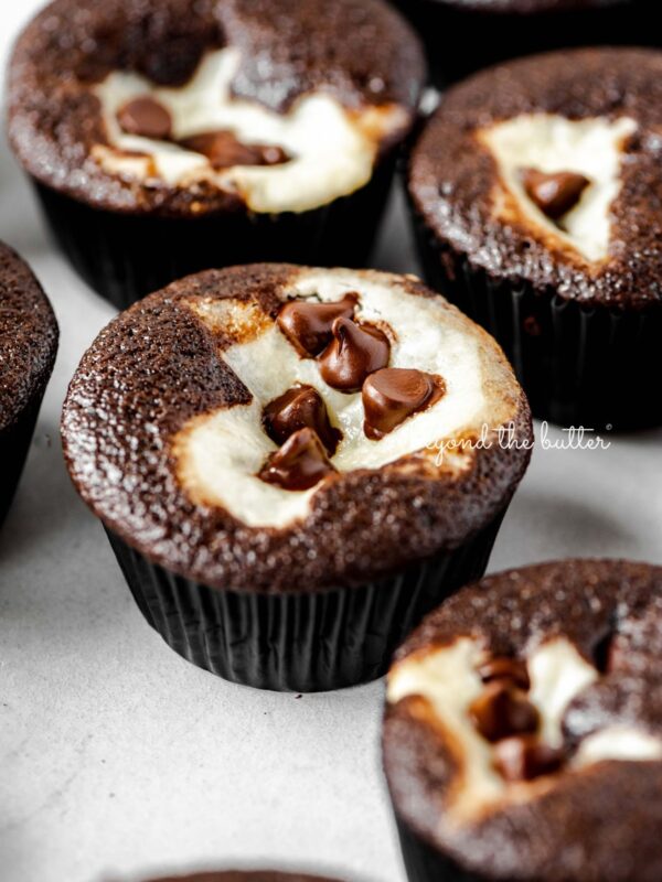 Cream cheese filled chocolate cupcakes topped with semi-sweet chocolate chips randomly placed on a light gray background.