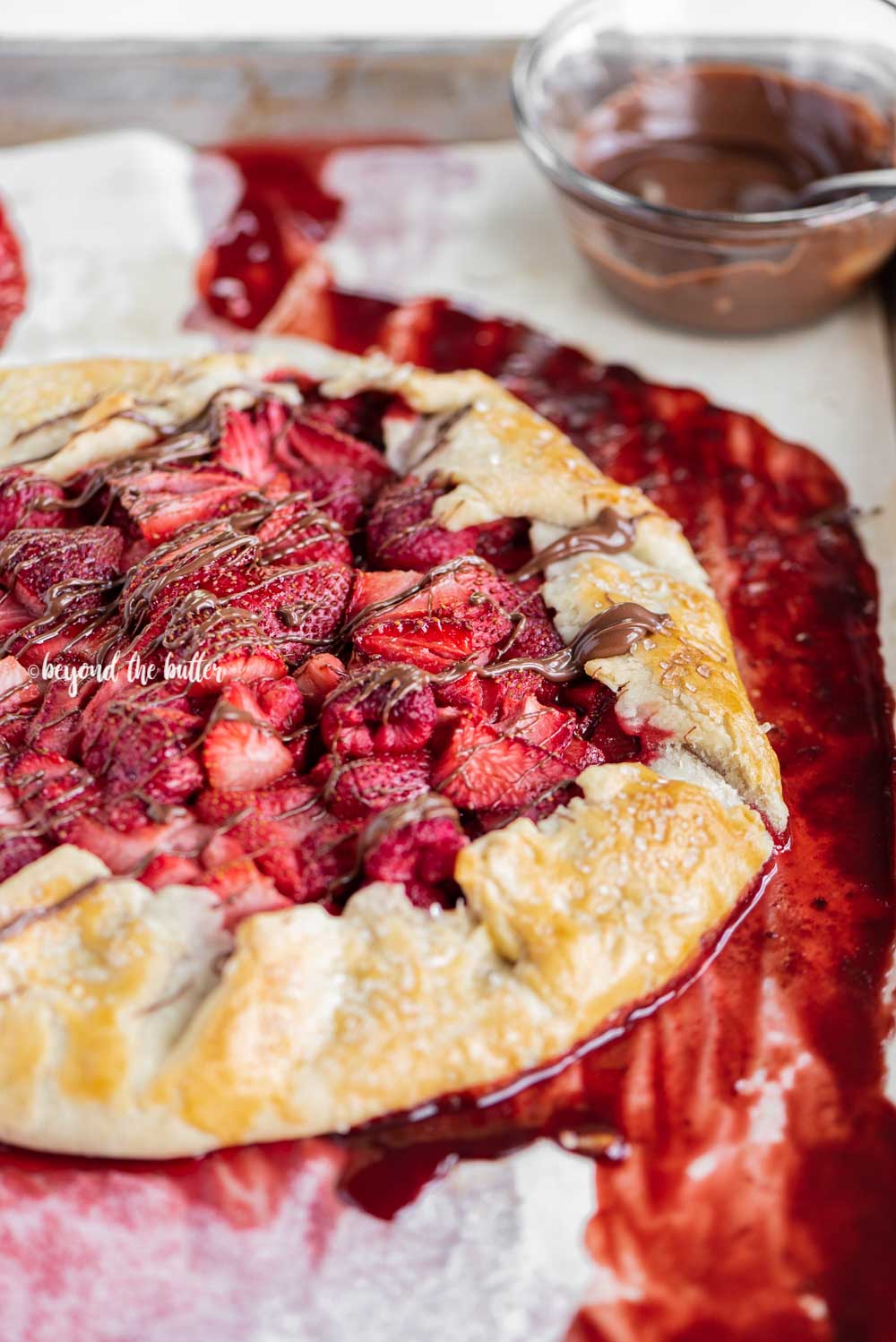 Angled close up image of a Berry Nutella Galette on a baking sheet with Nutella drizzled over the top | All Images © Beyond the Butter™