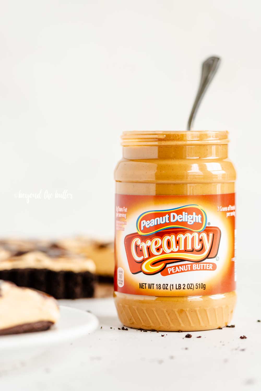 Front view of ALDI's opened jar of Peanut Delight Creamy Peanut Butter next to a chocolate peanut butter swirl tart | All Images © Beyond the Butter™