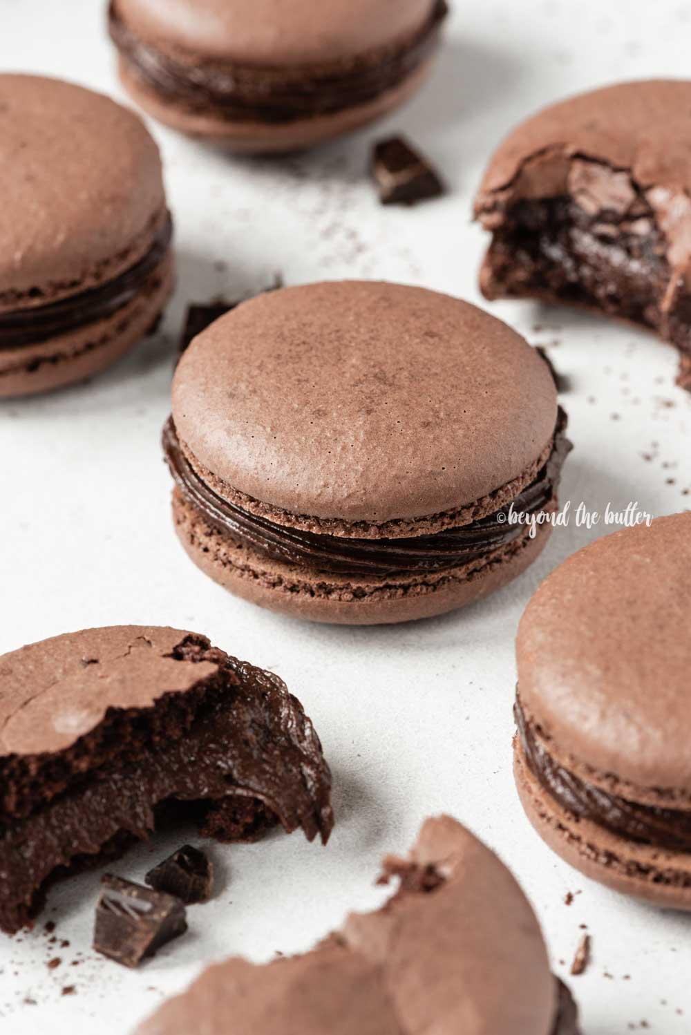 Scattered dark chocolate macarons with some broken or pulled apart | All Images © Beyond the Butter™