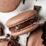 Overhead image of scattered dark chocolate macarons with close up and centered on its side.