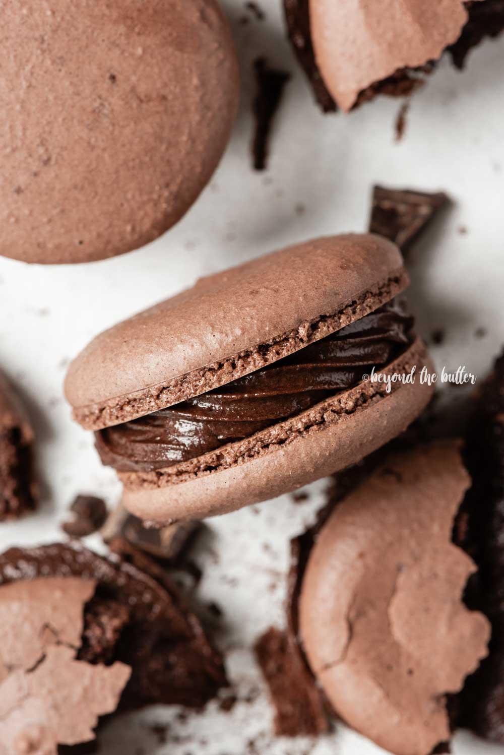 Overhead image of scattered dark chocolate macarons with close up and centered on its side | All Images © Beyond the Butter™