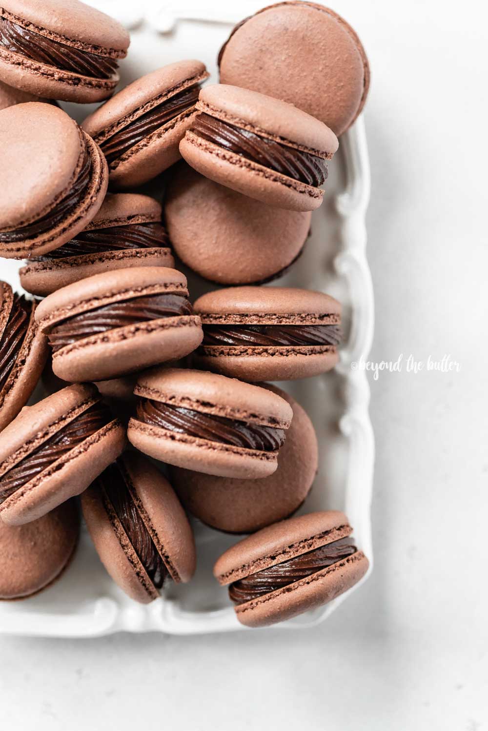 Overhead image of rectangular white plate full of chocolate macarons | All Images © Beyond the Butter™