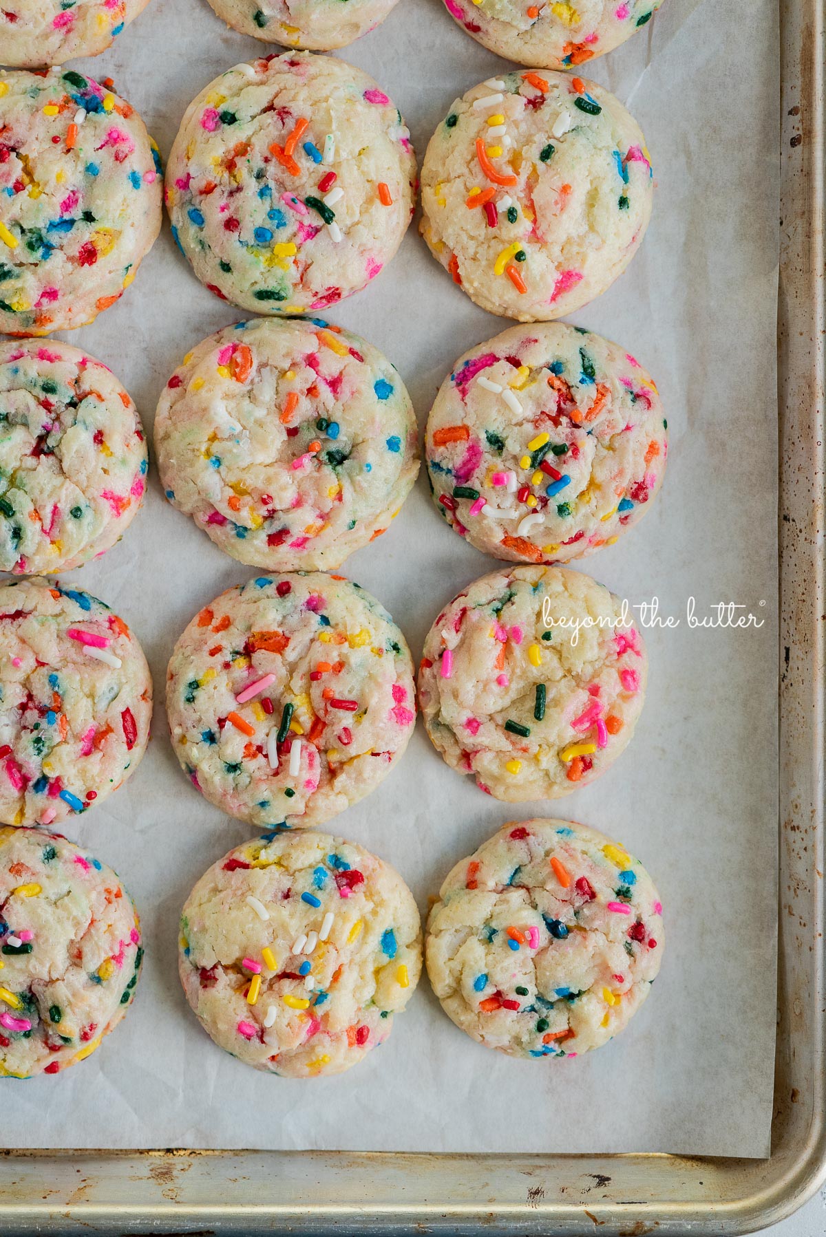 Funfetti gooey butter cookies on a white parchment paper-lined baking sheet.