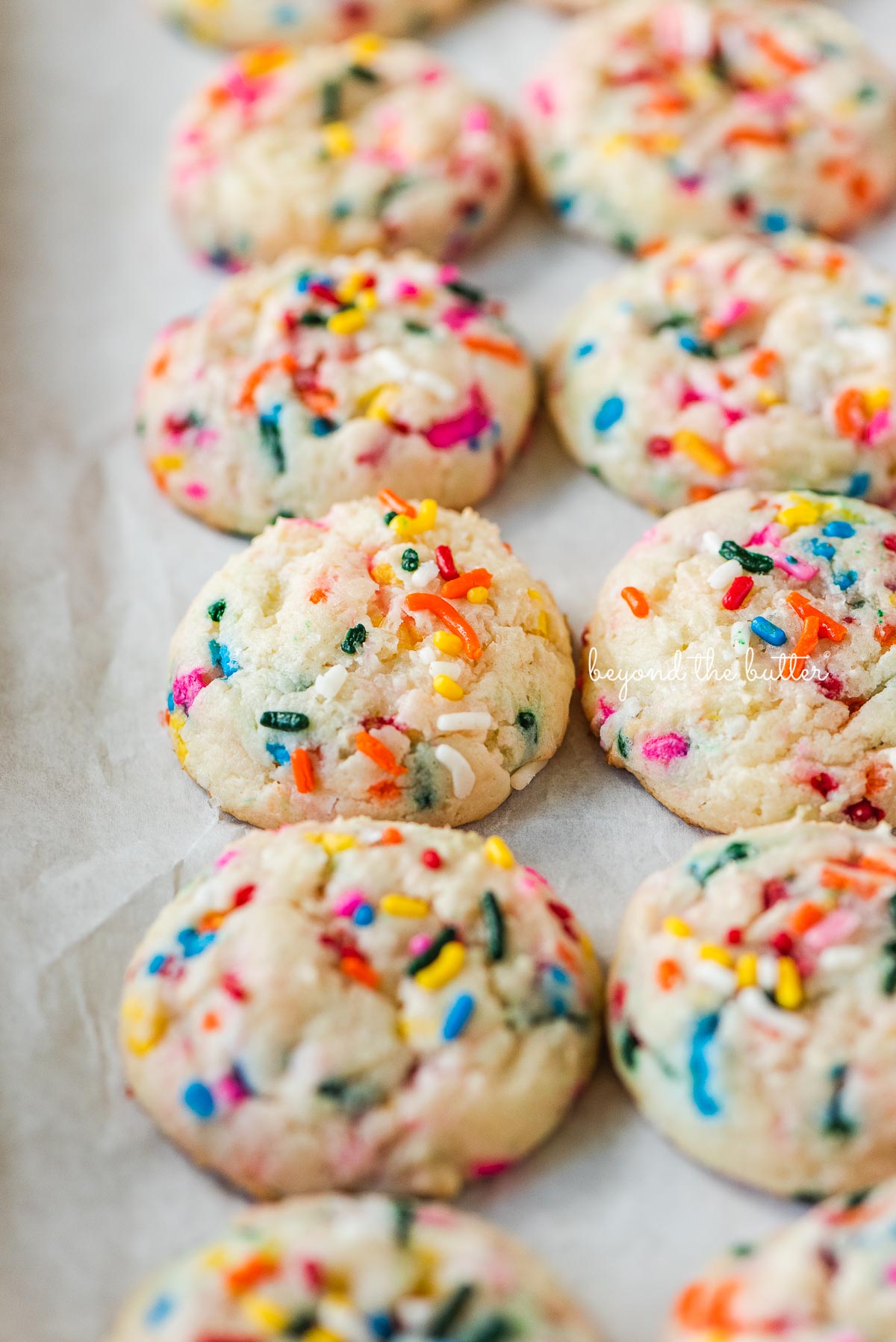 Parchment paper lined baking sheet with rows of gooey funfetti butter cookies.