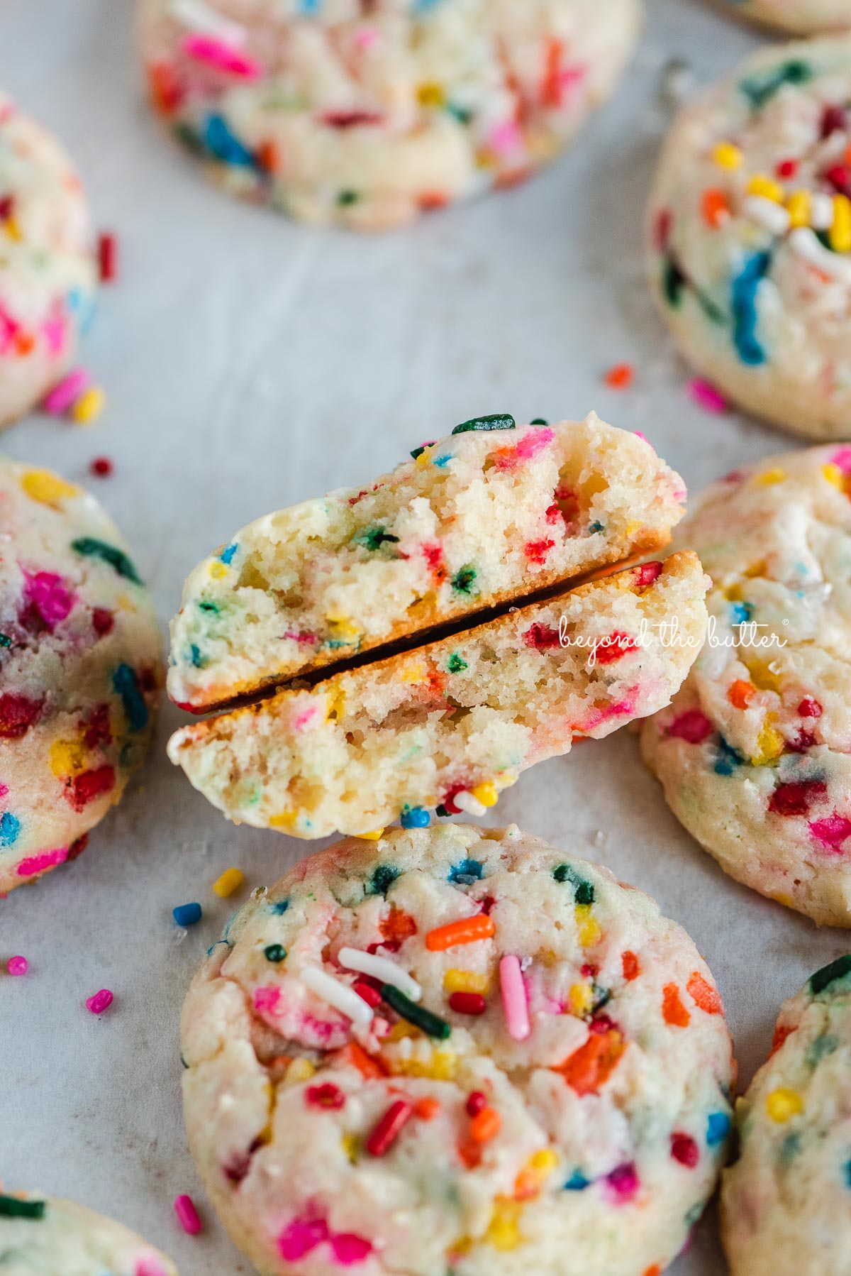 Funfetti butter cookies on a parchment paper lined baking sheet with the center cookie split in half.