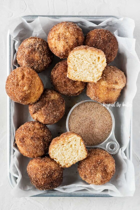 Overhead image of mini french breakfast puffs piled onto a parchment lined baking sheet with a bowl of cinnamon sugar | All Images © Beyond the Butter™