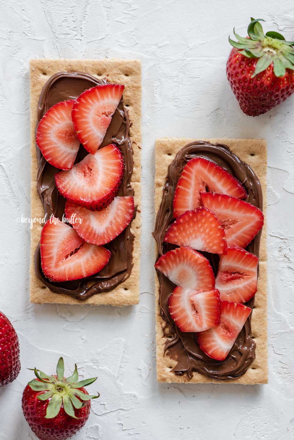 Image of strawberries and nutella spread over top of 2 graham crackers | All Images © Beyond the Butter®