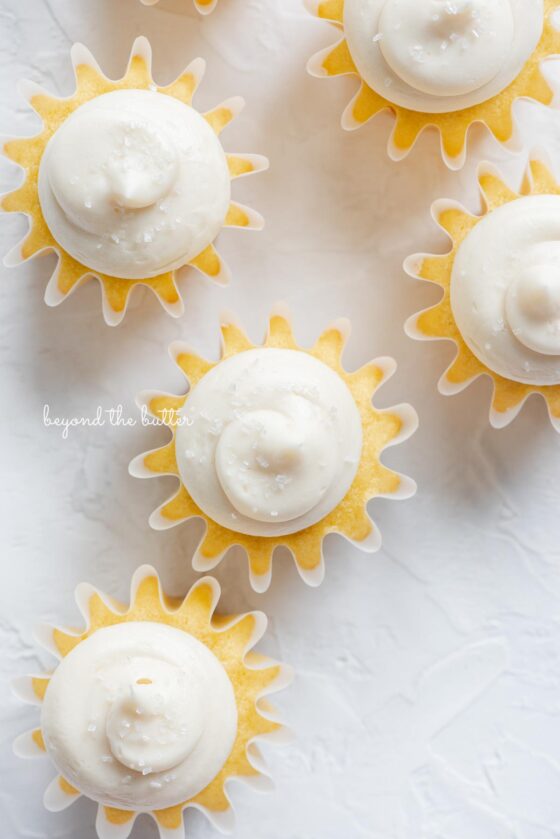 Overhead image of vanilla cupcakes with vanilla buttercream frosting sprinkled with sparkling sugar randomly placed on white background.