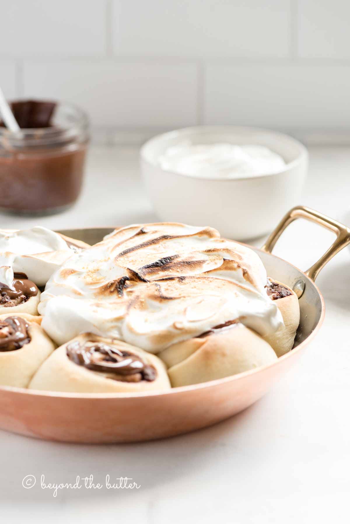Pan of s'mores rolls on a kitchen counter with bowl of marshmallow topping and melted chocolate | All Images © Beyond the Butter™