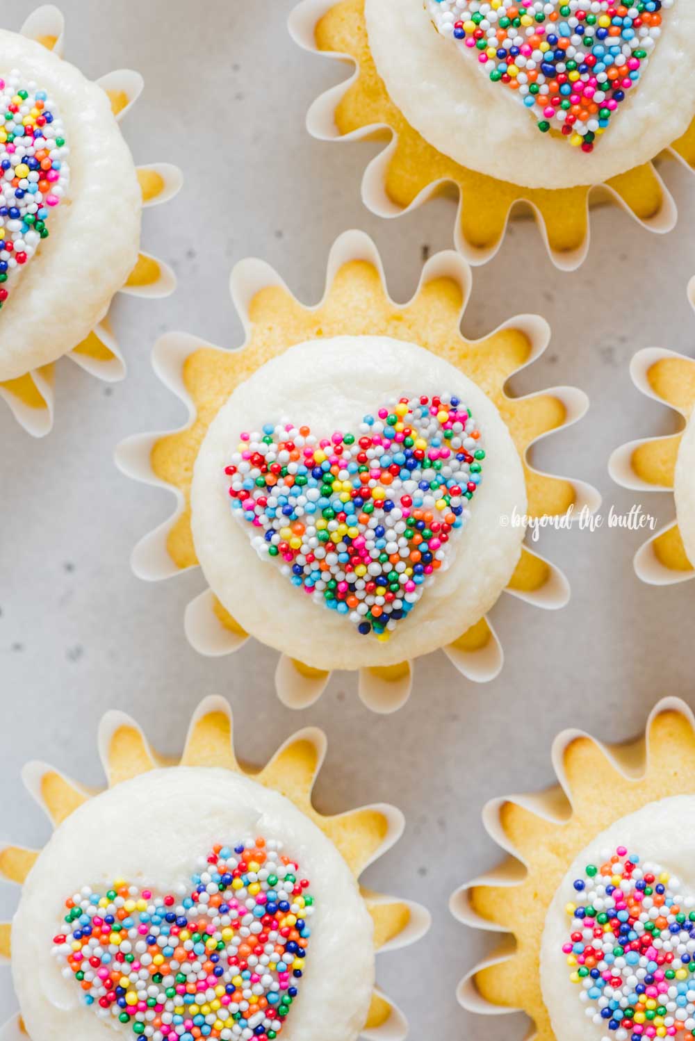 Overhead image of sprinkled heart cupcakes on white/grya background | All Images © Beyond the Butter™