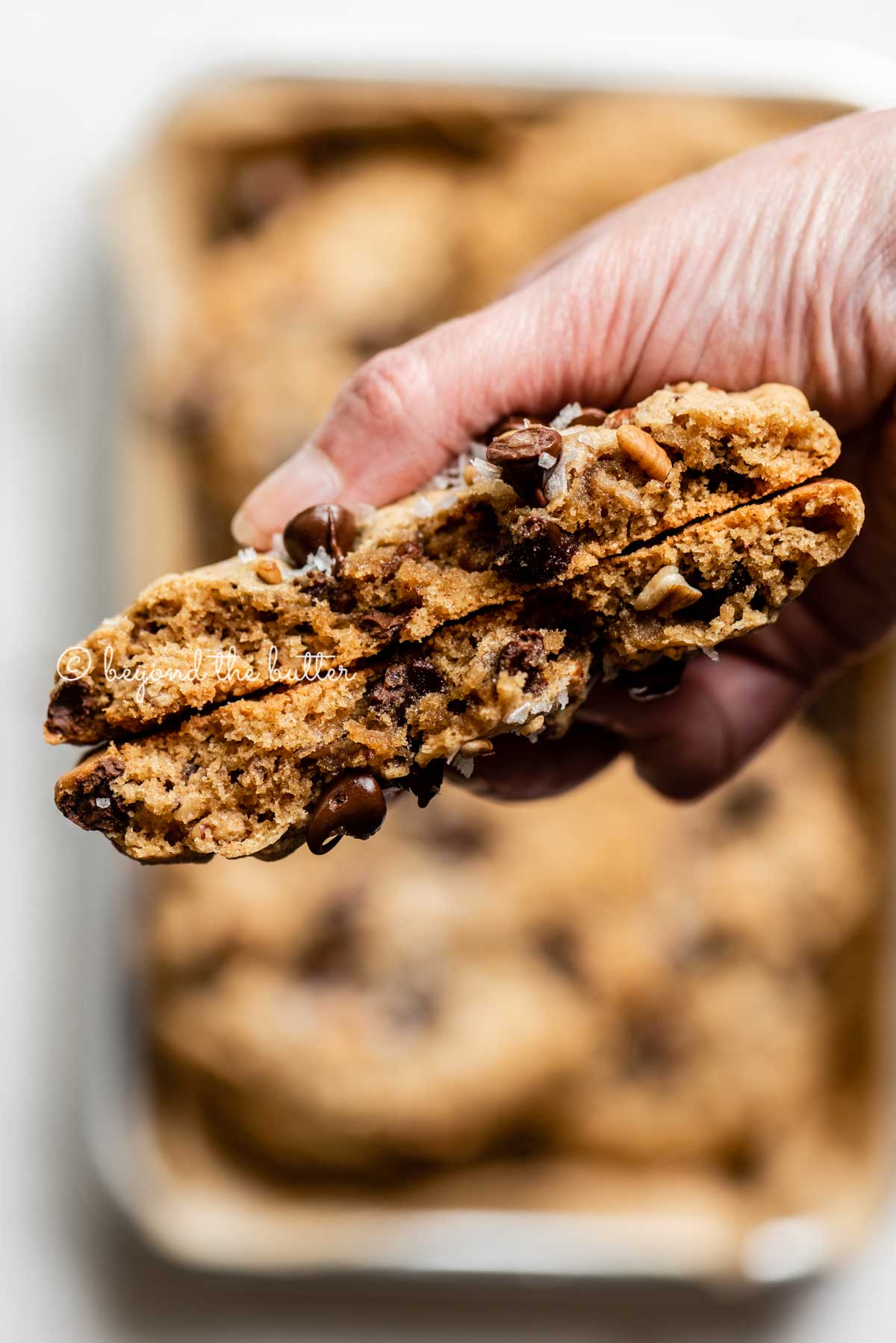 Hand holding a large almond butter chocolate chip pecan cookie that's been split in half | All images © Beyond the Butter™