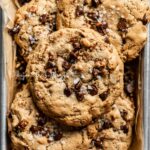 Large almond butter chocolate chip pecan cookies stacked on a parchment paper lined baking sheet | All Images © Beyond the Butter™