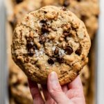 Hand holding a large almond butter chocolate chip pecan cookie.