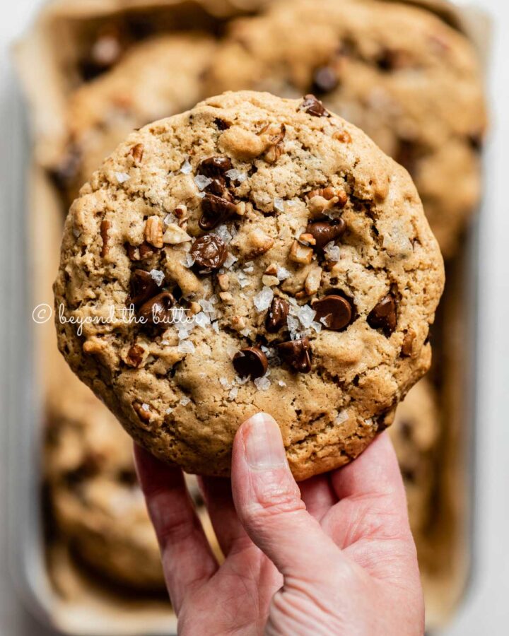 Hand holding a large almond butter chocolate chip pecan cookie.