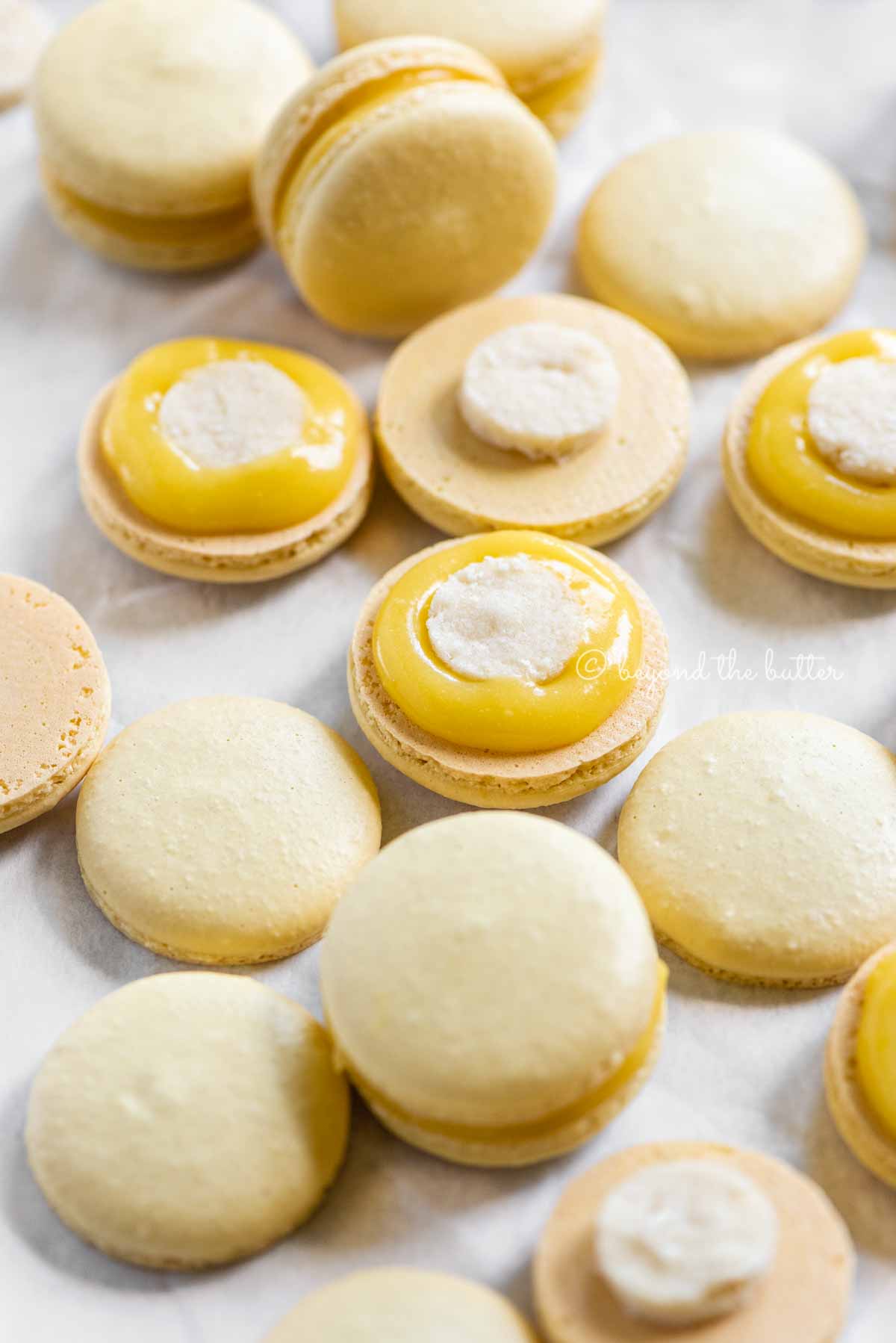 Angled image of lemon bar macarons half opened topped with shortbread crust centers and lemon curd filling | All Images © Beyond the Butter™