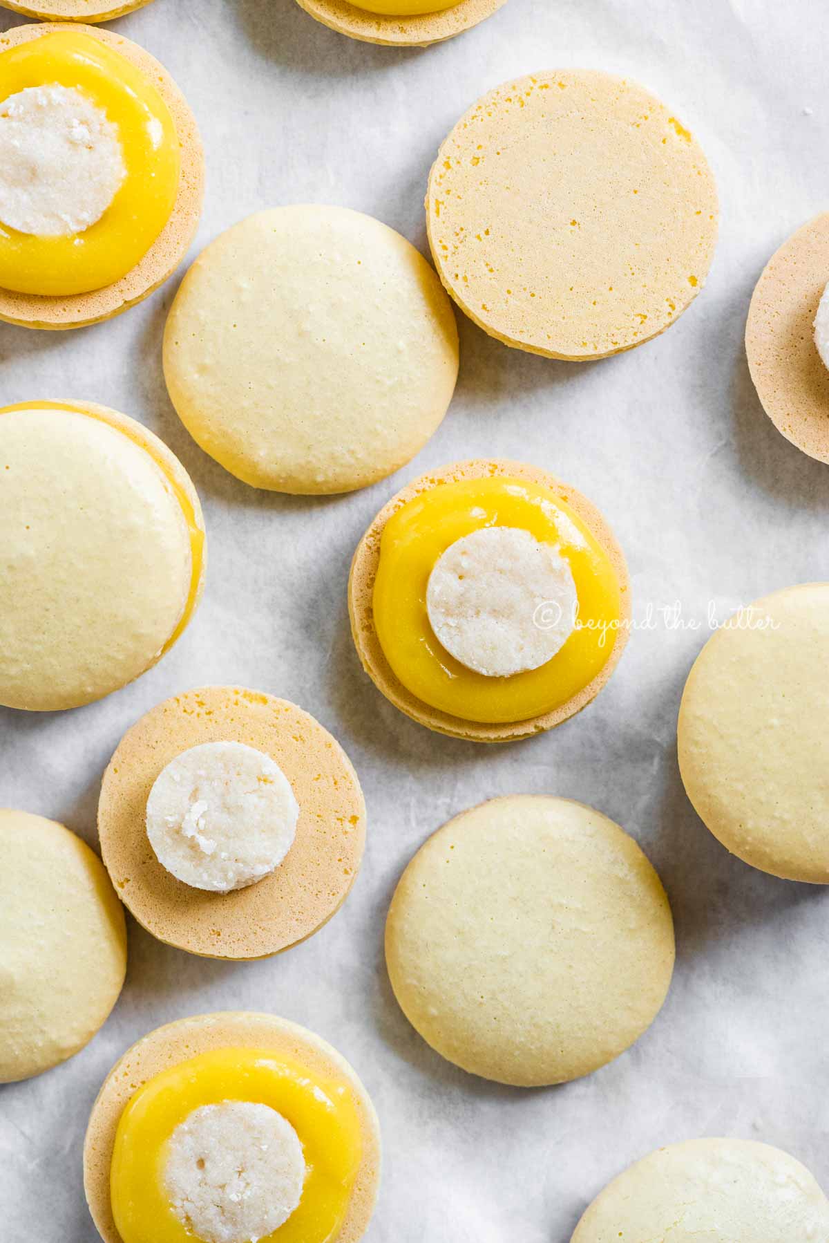 Overhead image of lemon bar macarons half opened topped with shortbread crust centers and lemon curd filling | All Images © Beyond the Butter™