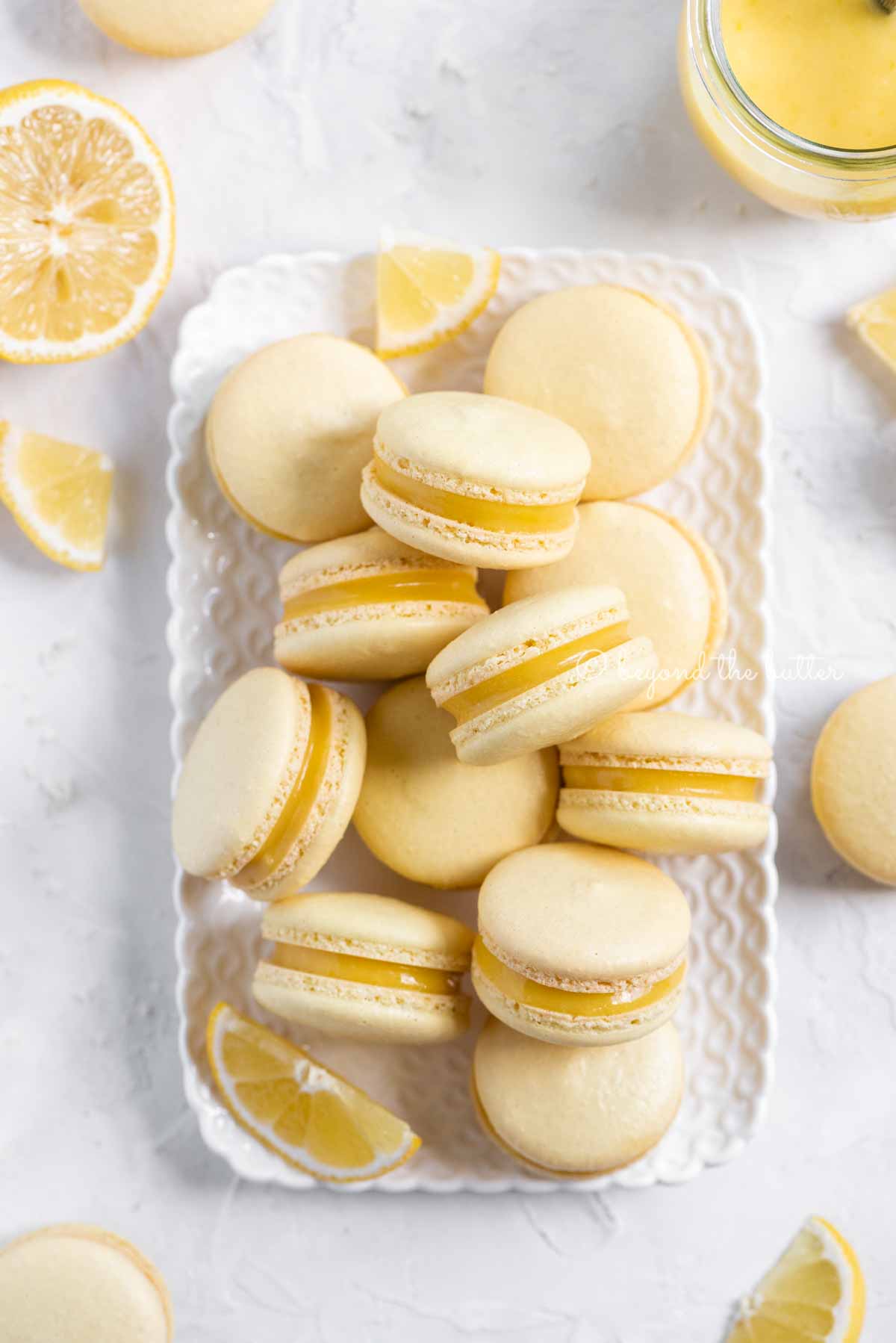 Overhead image of lemon bar macarons on a white dessert tray with lemon wedges | All Images © Beyond the Butter™