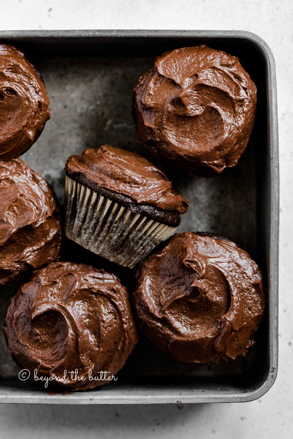 Overhead image of small batch chocolate cupcakes in vintage metal baking tin with one on its side | All Images © Beyond the Butter™