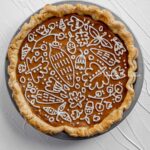 Pumpkin Pie decorated with cream cheese frosting on white textured background.
