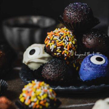 Plate of stacked homemade chocolate truffles with more around it on dark background | All Images © Beyond the Butter®