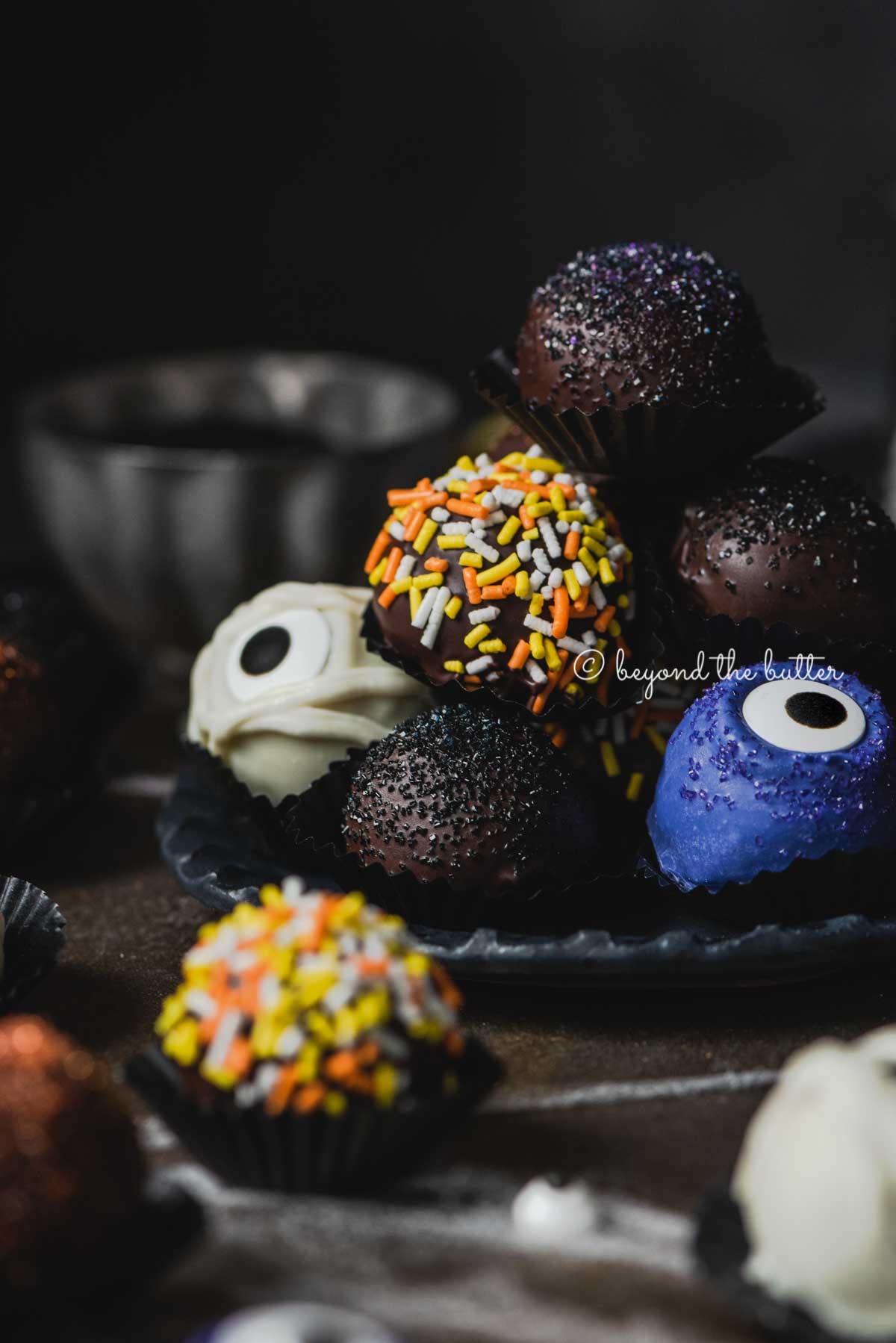Plate of stacked homemade chocolate truffles with more around it on dark background.