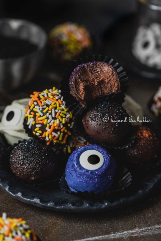 Plate of stacked homemade chocolate truffles with more around it on dark background | All Images © Beyond the Butter®