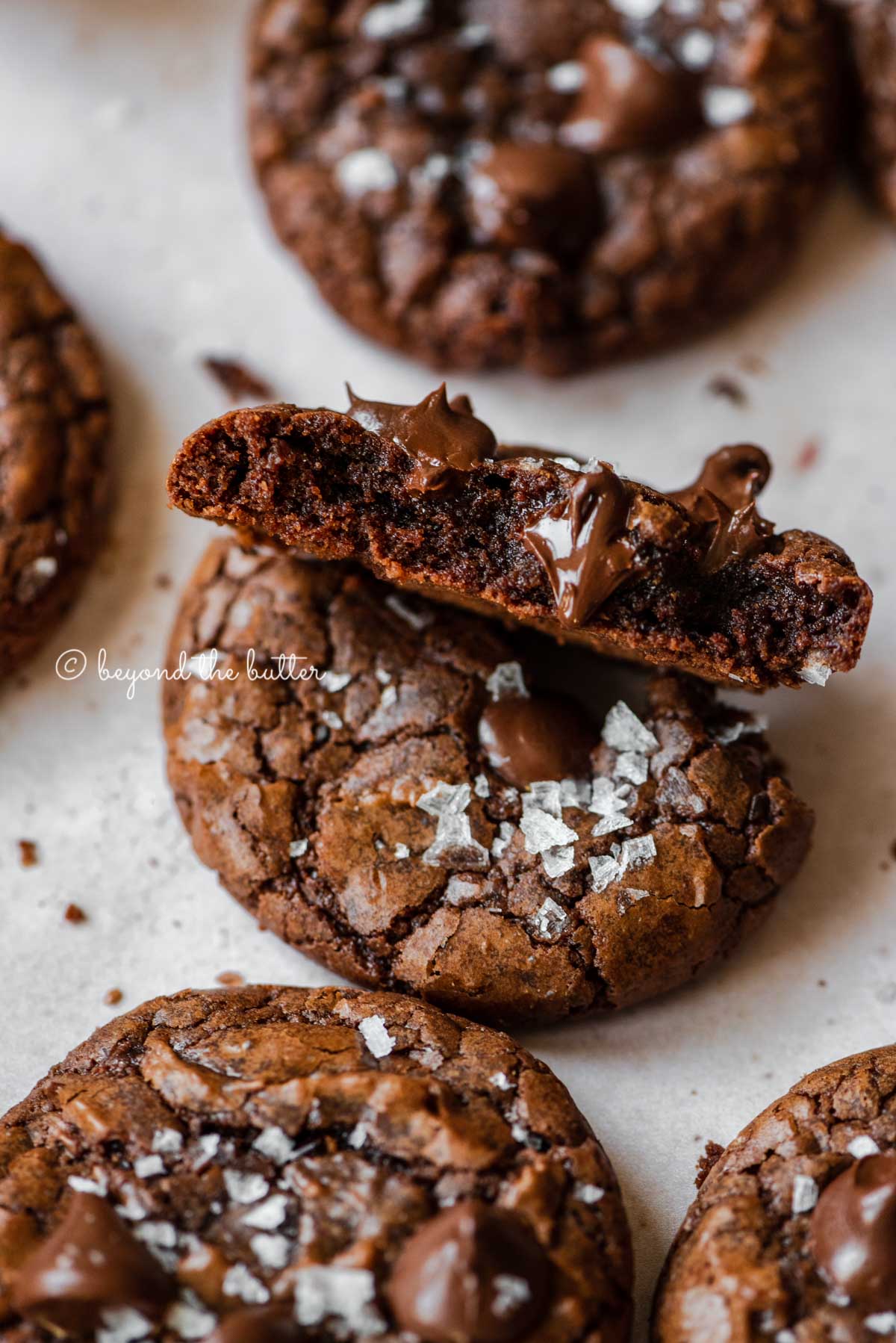 Salted brownie cookie split in half showing with melted chocolate chips peaking through | All Images © Beyond the Butter®