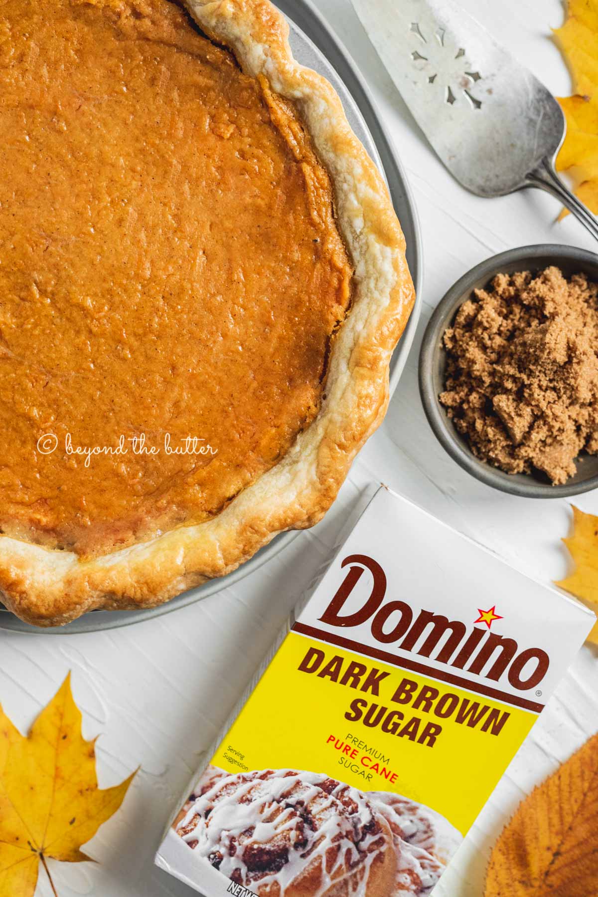 Overhead image of sweet potato pie with box of Domino® Dark Brown Sugar shown below it along with some colorful fall leaves | All Images © Beyond the Butter®
