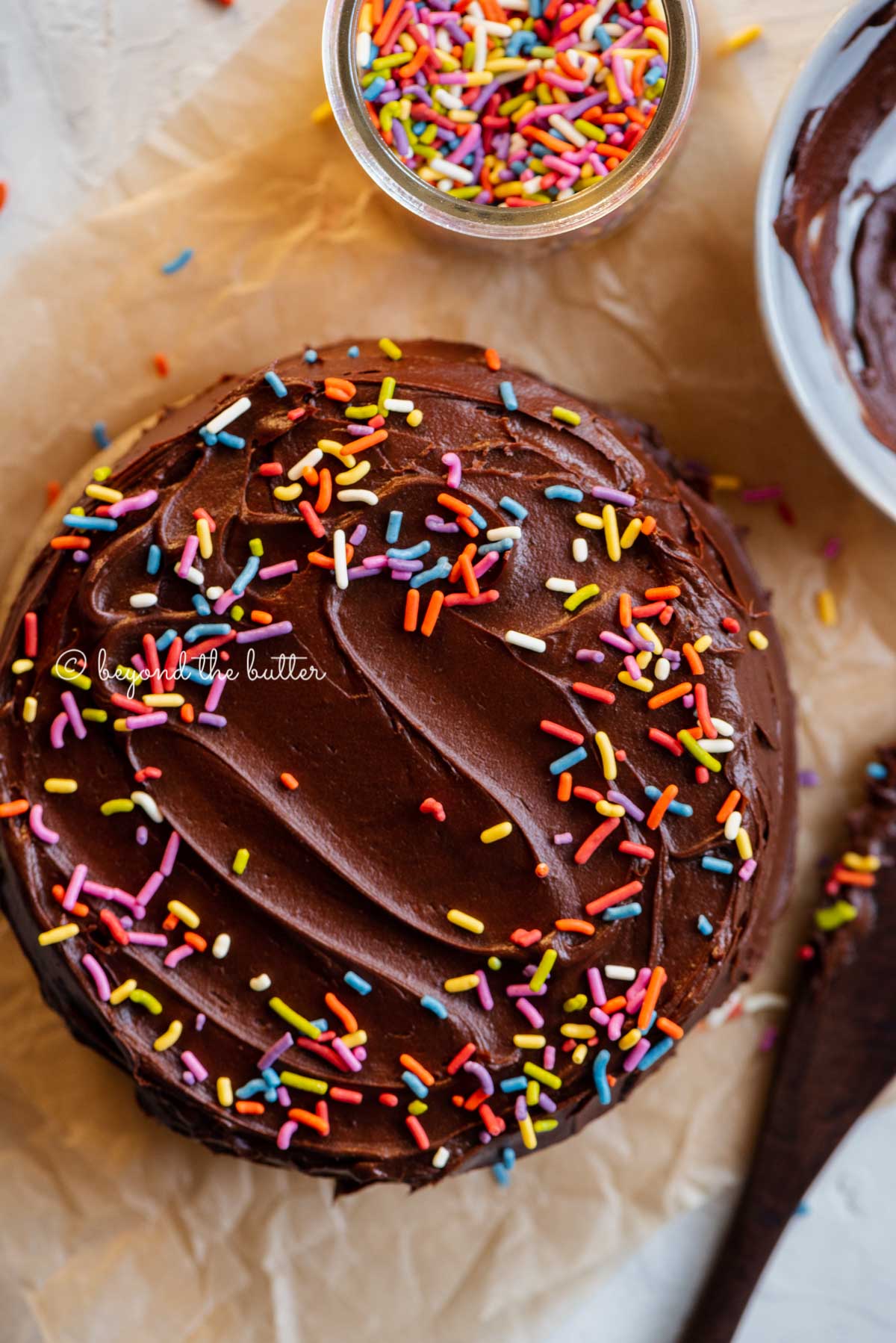 Overhead image of single layer chocolate cake with bowl of milk chocolate frosting | All Images © Beyond the Butter®