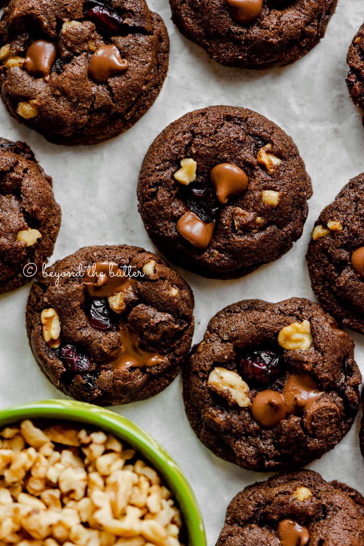 Dark chocolate cranberry walnut cookies with a small greeen bowl of chopped walnuts | All Images © Beyond the Butter®