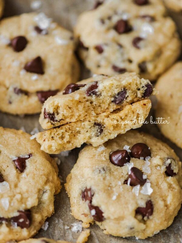 Chocolate chip shortbread cookies sprinkled with sea salt flakes on natural parchment paper with center cookie cut in half to see the center.
