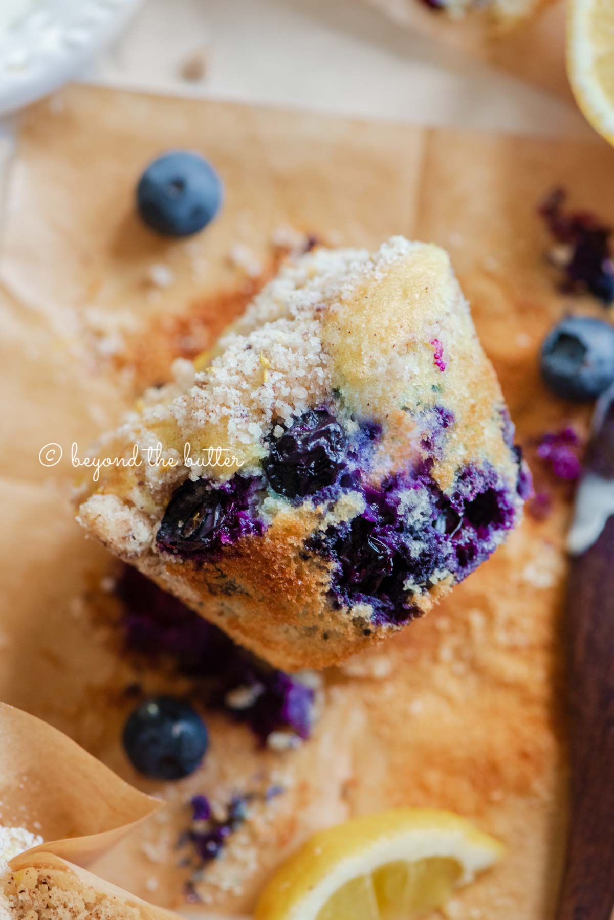 Unwrapped lemon blueberry streusel muffin with lemon wedges and blueberries around it | All images © Beyond the Butter®
