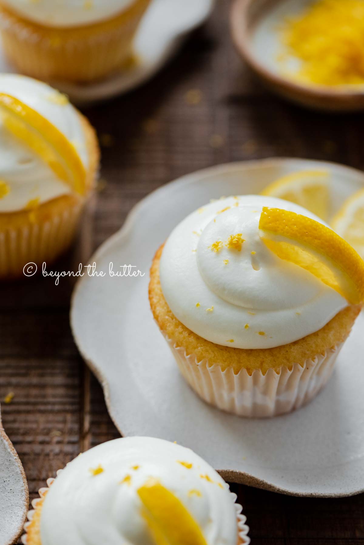 Lemon cupcakes with lemon cream cheese frosting garnished with lemons on small wavy dessert plates | All Images © Beyond the Butter®