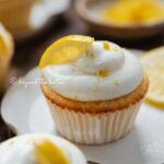 Lemon cupcakes with lemon cream cheese frosting garnished with lemons on small wavy dessert plates.