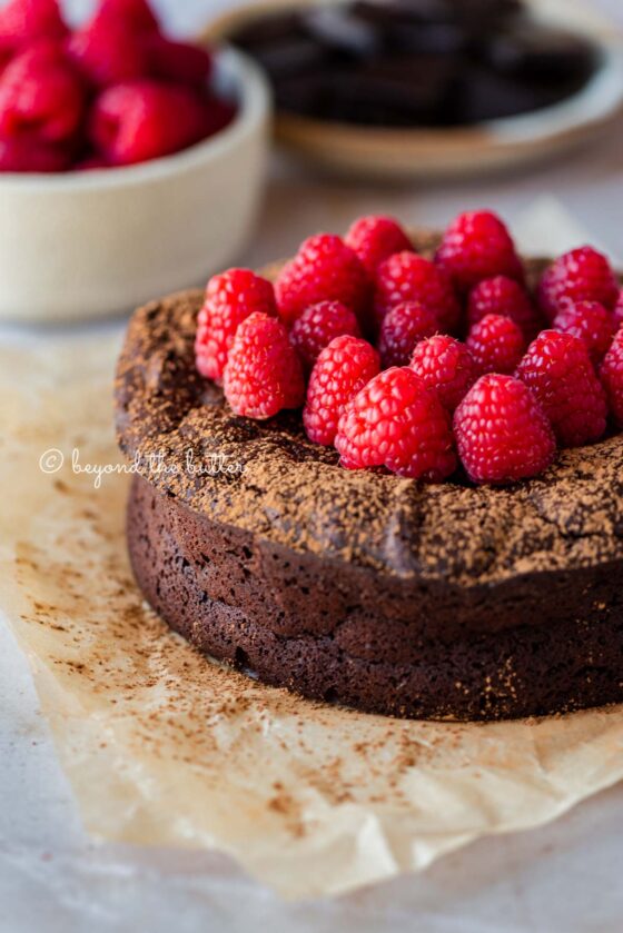 Small flourless chocolate cake topped with cocoa powder and fresh raspberries on parchment paper | All images © Beyond the Butter®